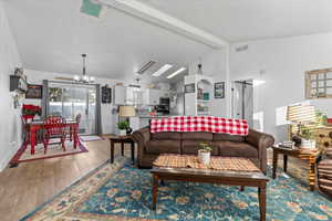 Living room featuring wood-type flooring, a notable chandelier, and vaulted ceiling with beams