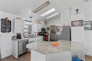 Kitchen with vaulted ceiling with skylight, pendant lighting, washing machine and dryer, white cabinetry, and stainless steel appliances