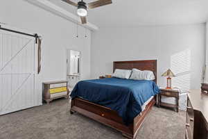 Carpeted bedroom featuring ceiling fan, connected bathroom, and a barn door