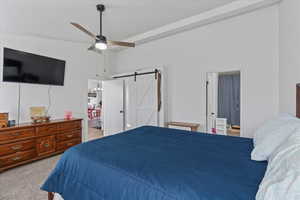 Carpeted bedroom featuring ceiling fan, connected bathroom, lofted ceiling, and a barn door