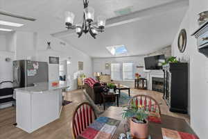 Dining space with a notable chandelier, a tile fireplace, lofted ceiling with skylight, and light hardwood / wood-style flooring