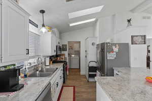 Kitchen with white cabinetry, stainless steel appliances, decorative light fixtures, lofted ceiling with skylight, and sink