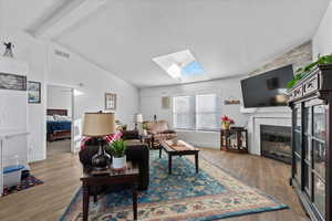 Living room with lofted ceiling with skylight, wood-type flooring, and a tiled fireplace