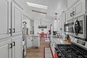 Kitchen featuring light stone countertops, white cabinets, stainless steel appliances, sink, and a notable chandelier