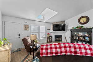 Living room featuring lofted ceiling with skylight, a tile fireplace, and hardwood / wood-style floors