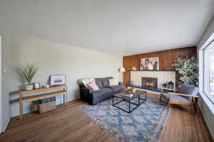 Living room with a brick fireplace, dark wood-type flooring, a wealth of natural light, and a textured ceiling