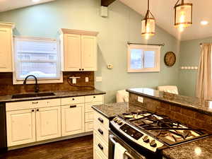 Kitchen featuring decorative backsplash, gas stove, decorative light fixtures, vaulted ceiling with beams, and sink