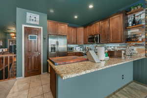 Kitchen with light tile patterned flooring, stainless steel appliances, kitchen peninsula, and light stone countertops