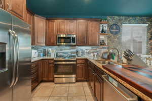 Kitchen featuring wooden counters, decorative backsplash, sink, stainless steel appliances, and light tile patterned floors