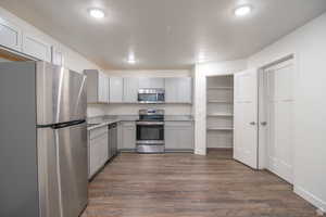 Kitchen with a textured ceiling, dark wood-type flooring, appliances with stainless steel finishes, and gray cabinets