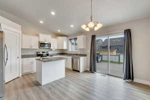 Kitchen with white cabinets, appliances with stainless steel finishes, a center island, decorative light fixtures, and dark stone counters