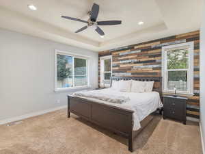 Bedroom featuring ceiling fan, a raised ceiling, wood walls, and multiple windows