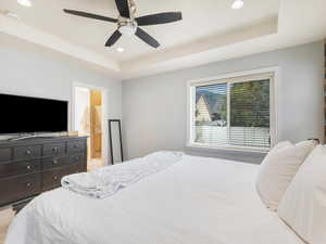 Bedroom featuring ceiling fan, a tray ceiling, and ensuite bathroom