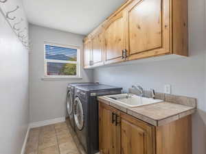 Washroom with light tile patterned floors, cabinets, washer and dryer, and sink