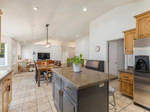 Kitchen featuring a center island, lofted ceiling, dark stone counters, stainless steel fridge, and light tile patterned flooring