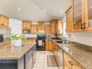 Kitchen featuring a kitchen island, sink, appliances with stainless steel finishes, custom range hood, and light stone counters