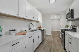 Kitchen with light wood-type flooring, appliances with stainless steel finishes, white cabinets, and sink