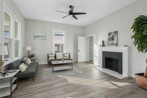 Living room featuring light wood-type flooring, ceiling fan, and a fireplace