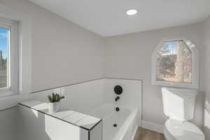 Bathroom with toilet, a bathing tub, and hardwood / wood-style flooring