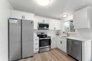 Kitchen featuring sink, white cabinetry, light hardwood / wood-style flooring, and stainless steel appliances