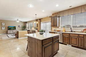 Kitchen featuring ceiling fan with notable chandelier, pendant lighting, a center island, sink, and stainless steel dishwasher