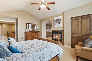 Primary suite bedroom featuring ceiling fan, a multi sided fireplace, connected bathroom, and vaulted ceiling