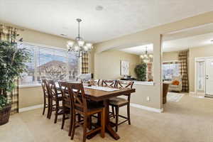 Carpeted dining room featuring a notable chandelier, a wealth of natural light, and a textured ceiling