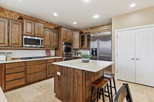 Kitchen featuring backsplash, a center island, appliances with stainless steel finishes, a kitchen breakfast bar, and light tile patterned floors