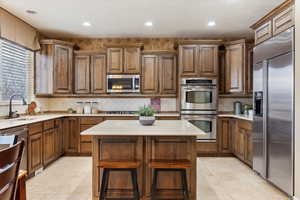 Kitchen with a kitchen bar, stainless steel appliances, backsplash, sink, and a center island