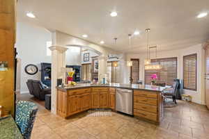 Kitchen with ornate columns, kitchen peninsula, decorative light fixtures, stainless steel dishwasher, and sink