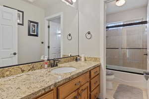 Full bathroom with toilet, bath / shower combo with glass door, tile patterned floors, and vanity