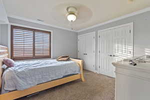 Bedroom with ceiling fan, two closets, crown molding, and carpet flooring