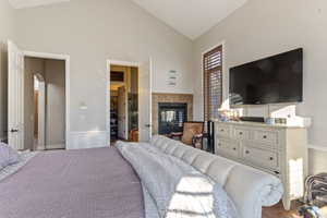 Bedroom with high vaulted ceiling, hardwood / wood-style flooring, and a fireplace