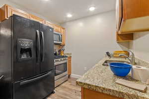 Kitchen featuring light wood-type flooring, light stone countertops, appliances with stainless steel finishes, and sink