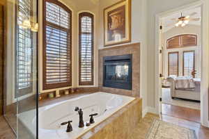 Bathroom with tiled bath, a wealth of natural light, ceiling fan, and tile patterned flooring