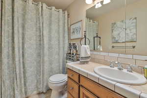 Bathroom with tile patterned flooring, vanity, a shower with curtain, tasteful backsplash, and toilet