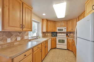 Kitchen with light tile patterned floors, decorative backsplash, sink, and white appliances