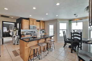 Kitchen with pendant lighting, appliances with stainless steel finishes, a center island with sink, and light tile patterned flooring