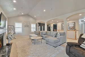 Living room with light carpet, a premium fireplace, lofted ceiling, and a textured ceiling