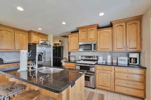 Kitchen featuring a kitchen bar, stainless steel appliances, backsplash, a kitchen island with sink, and light tile patterned flooring