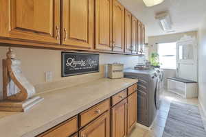 Clothes washing area featuring a textured ceiling, cabinets, light tile patterned floors, and washing machine and clothes dryer