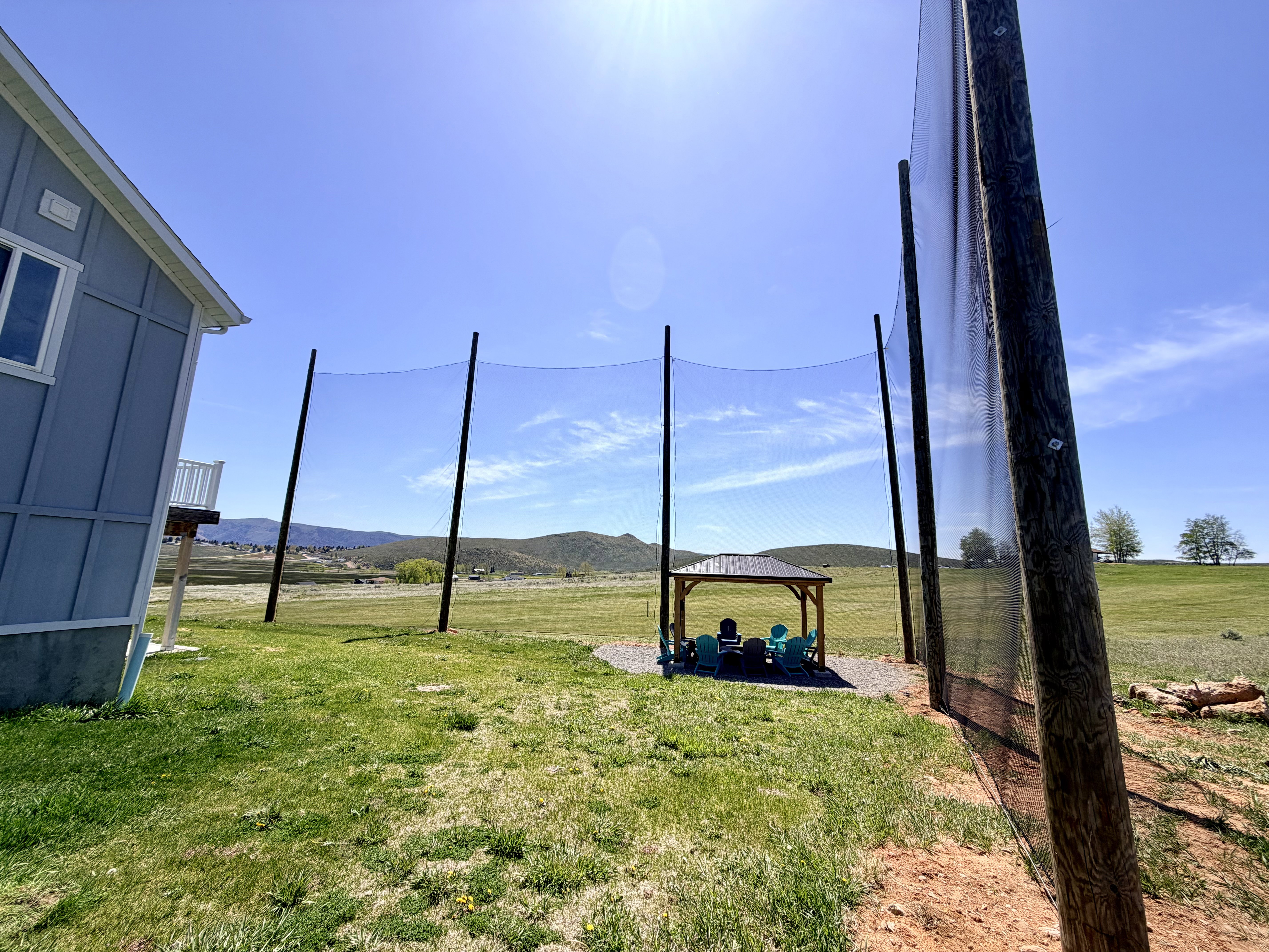 Outdoor recreation area featuring a driving range net, covered gazebo, and gravel patio
