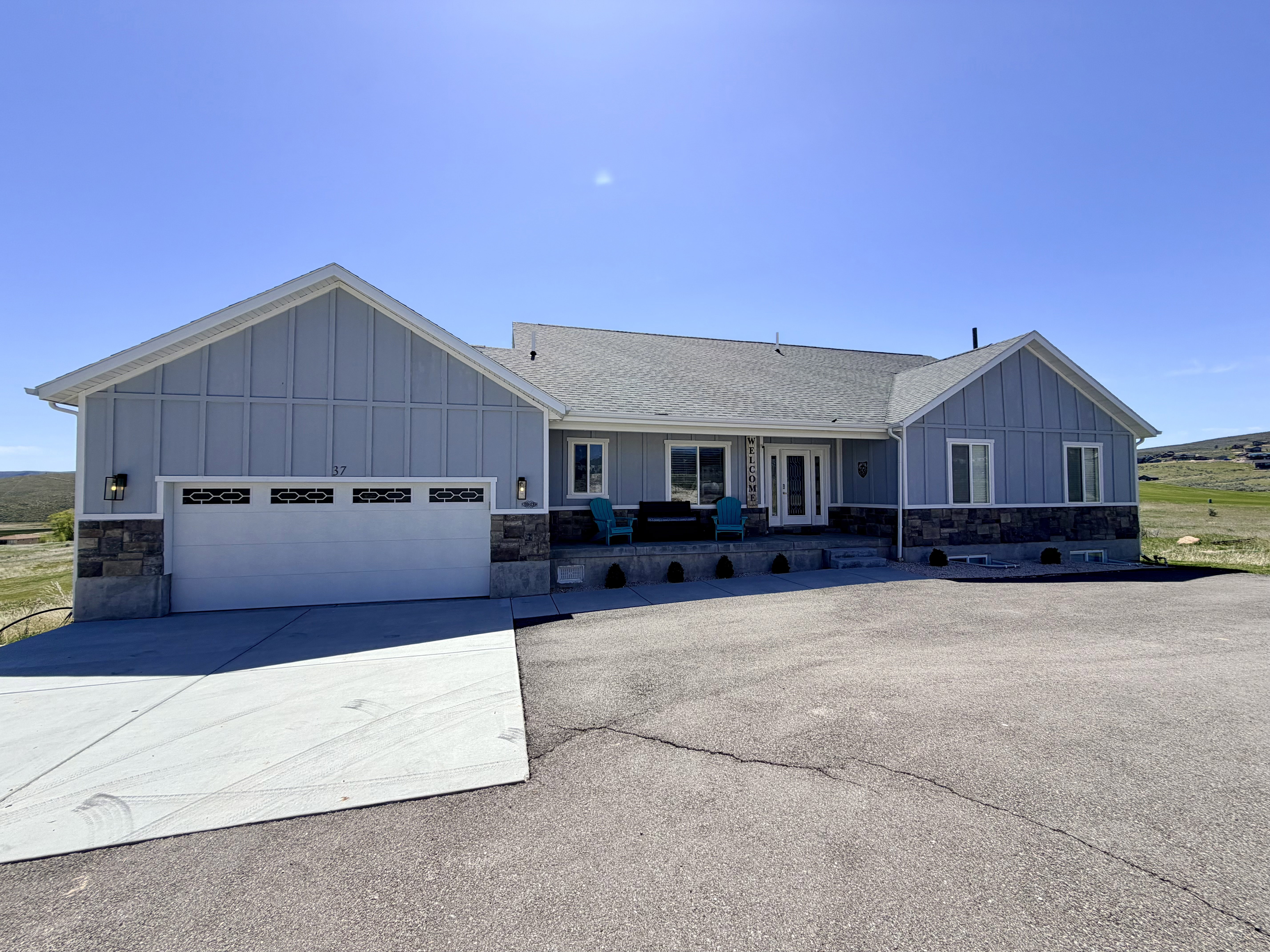 Exterior featuring light blue vertical siding, a stone veneer foundation, a shingle roof, a two-car garage with decorative windows, and a covered front porch