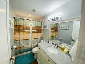 Full bathroom featuring toilet, vanity, and shower / bathtub combination with curtain