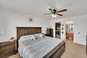 Carpeted bedroom featuring a walk in closet, ceiling fan, and ensuite bath