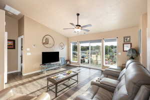 Living room featuring lofted ceiling, wood-type flooring, a textured ceiling, and ceiling fan