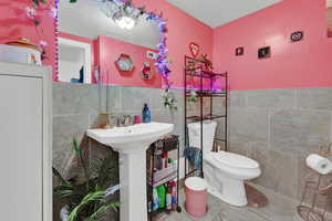 Bathroom with toilet, tile walls, tile patterned floors, and sink