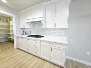 Kitchen featuring stainless steel gas stovetop, white cabinetry, decorative backsplash, custom range hood, and light hardwood / wood-style flooring