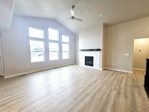 Unfurnished living room featuring ceiling fan, lofted ceiling, a tiled fireplace, and light hardwood / wood-style floors