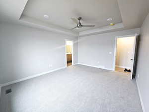 Unfurnished bedroom with ceiling fan, ensuite bath, light carpet, and a tray ceiling